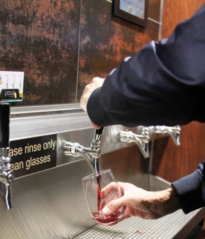 A patron pours themselves a glass of wine from a self-pour tap wall