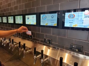 A PourMyBeer card is held up at a self-pour station in a restaurant