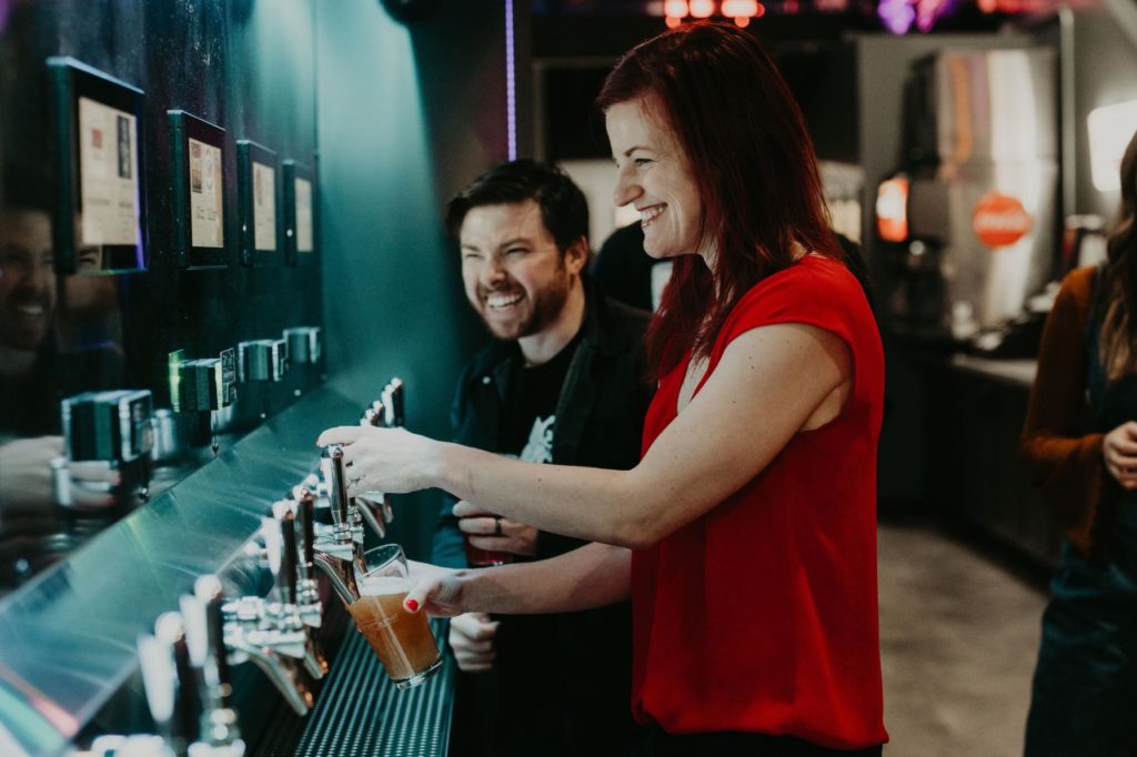 Two people smiling inside a restaurant as they use self-pour beer taps