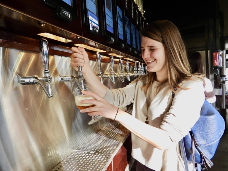 A smiling patron uses a PourMyBeer tap to fill a glass