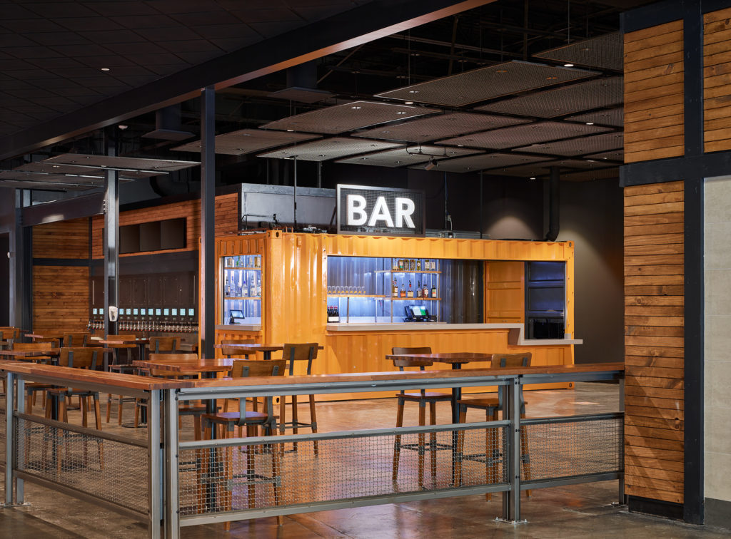 A small dining area and a self-pour tap setup with a neon "Bar" sign above it